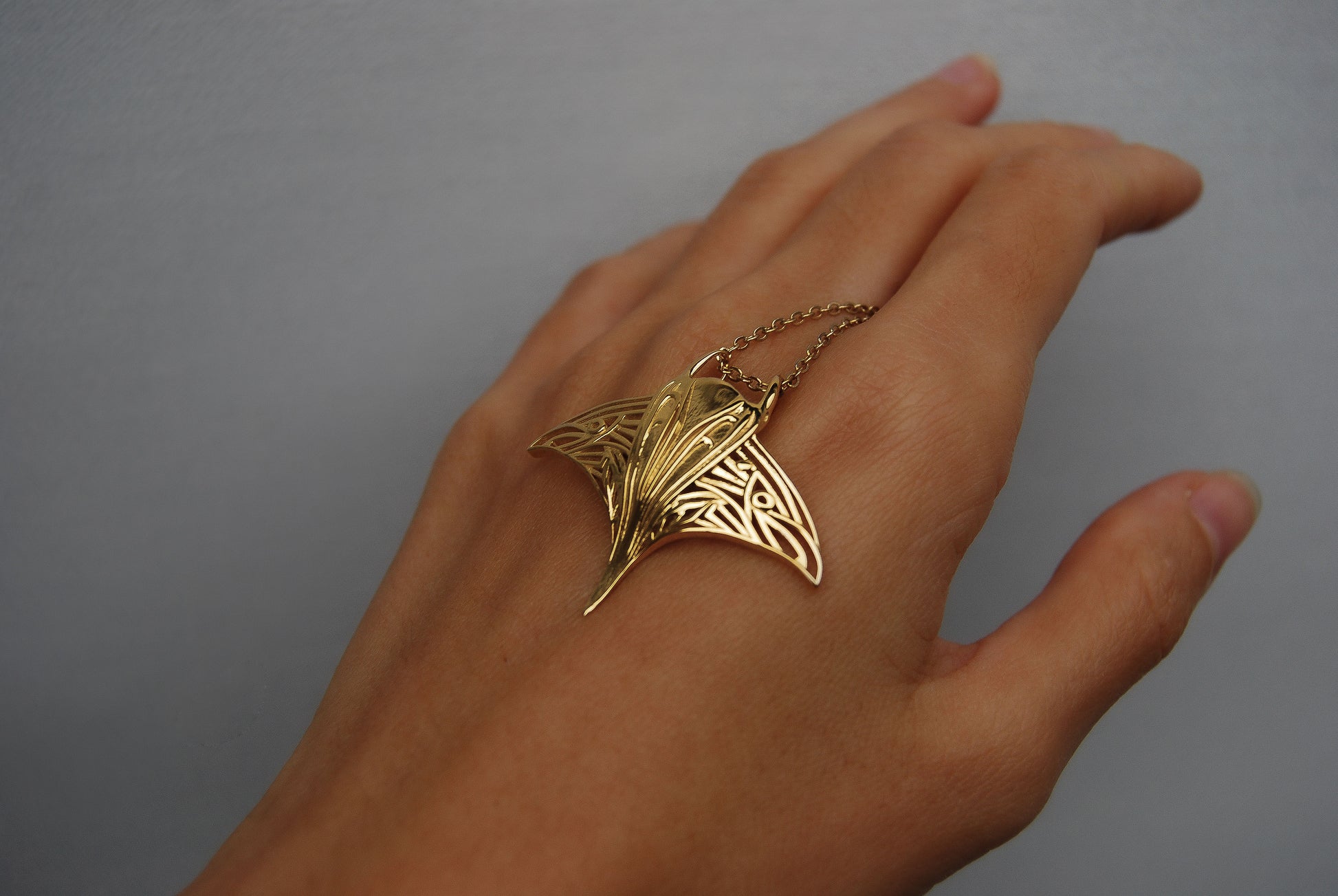 Side profile of gold manta ray pendant, showing sculptural wings and fantasy-inspired cut-outs.