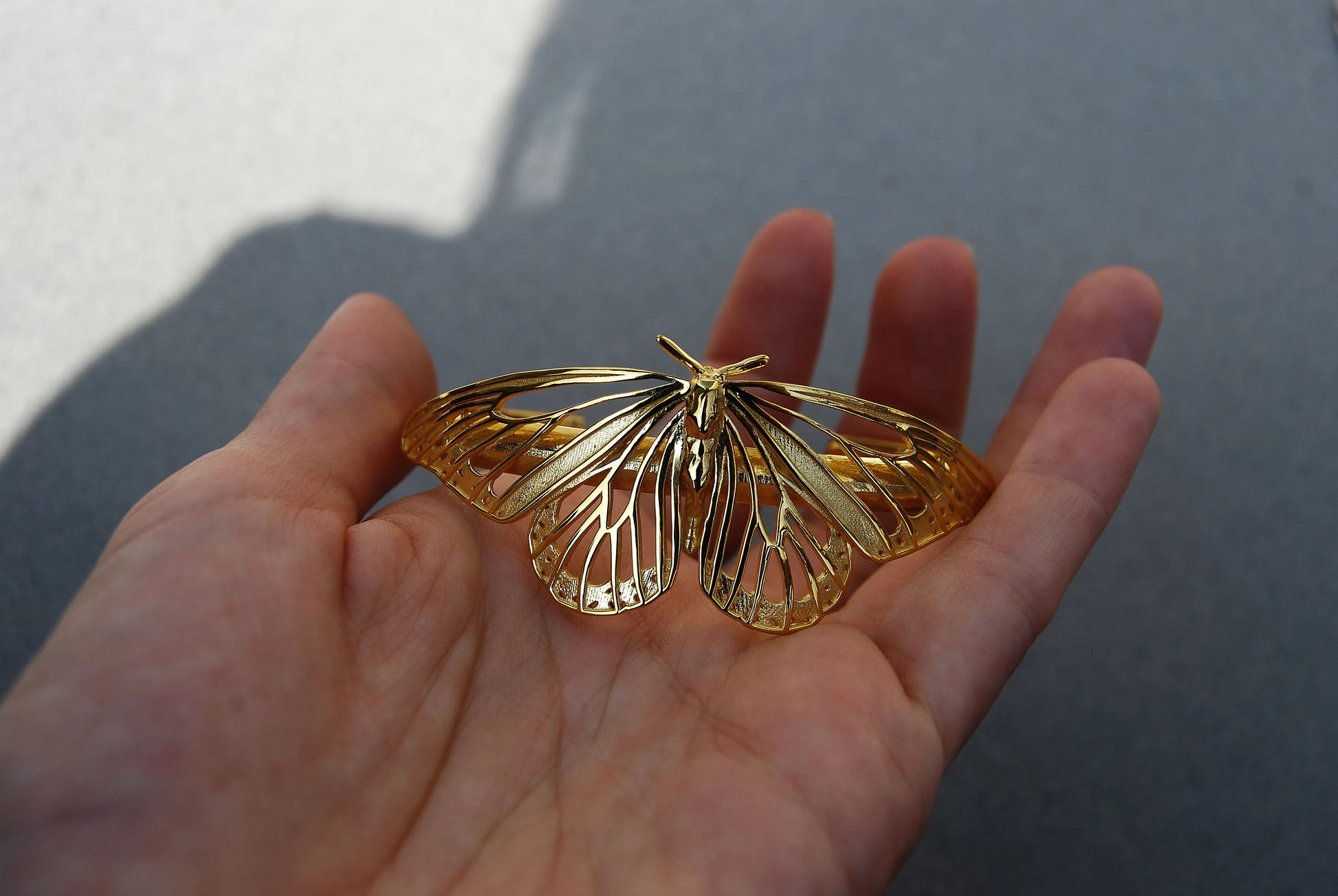 14K gold-plated Monarch Butterfly Bracelet held in hand, showing polished finish and delicate wing structure.