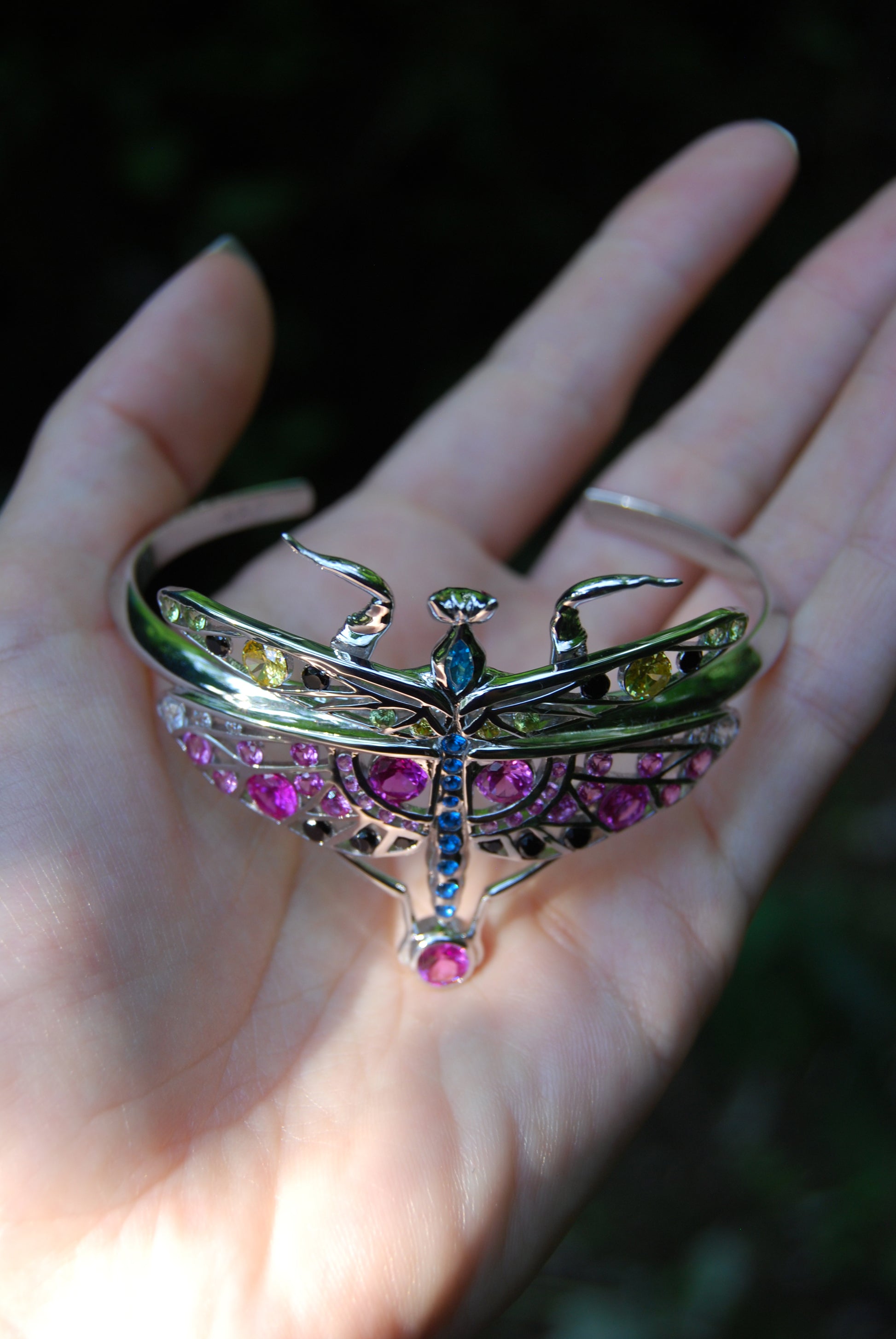 Top view of sterling silver mantis bracelet with enamel and zirconia stones displayed outdoors on natural surface