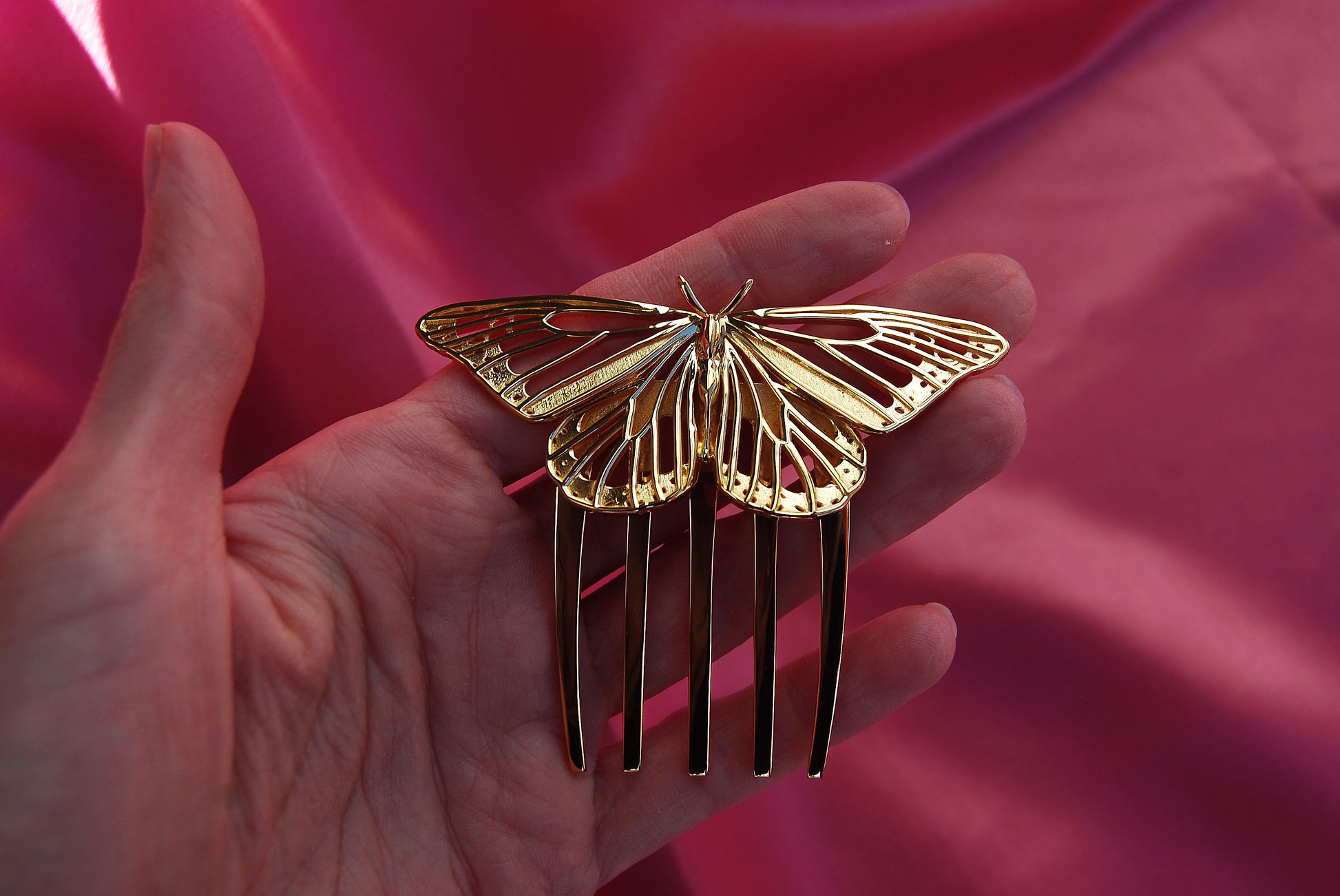Monarch Butterfly hair comb crafted in 14k gold plated brass, resting on a soft silk background. The delicate cut-out wings and luminous gold finish highlight the comb’s intricate design and luxurious craftsmanship.