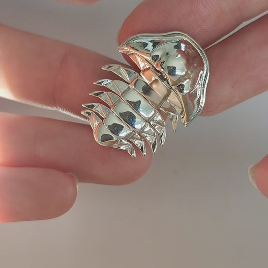 Hands gently manipulate the sterling silver articulated trilobite pendant against a white background, showcasing the fluid motion of its segmented body. Each joint flexes smoothly, highlighting the pendant’s lifelike mobility and intricate craftsmanship inspired by ancient marine fossils.