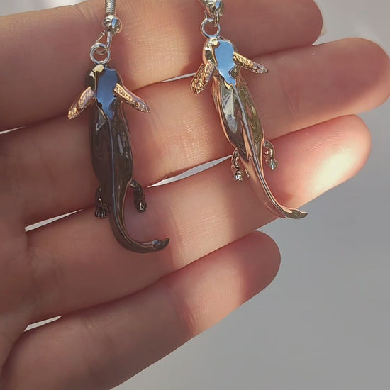 Video showing the Axolotl Drop Earrings held in hand, rotating to reveal their sculpted details, contrasting finishes, and shimmering rose gold gills.