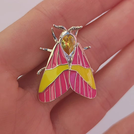 Video showing Rosy Maple Moth pendant held in hand, highlighting enamel and gemstone details