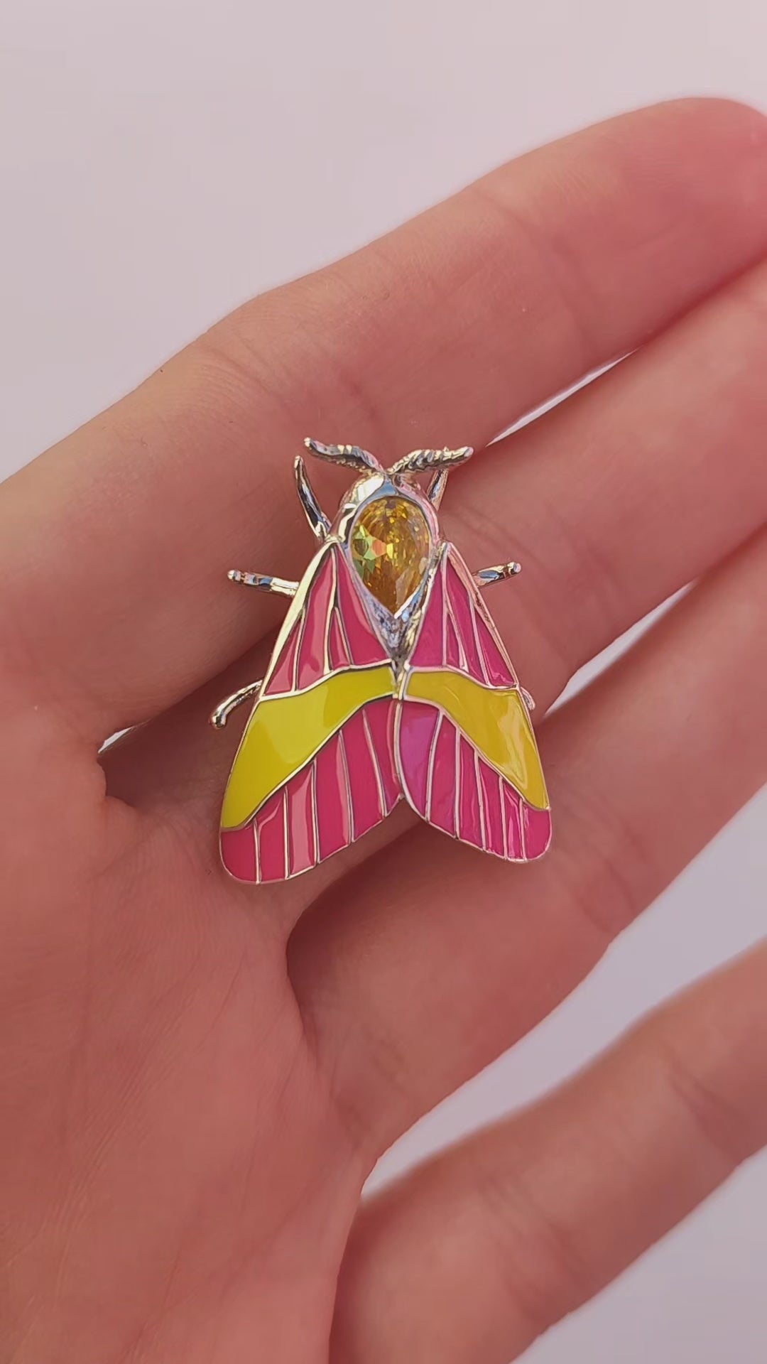 Video showing Rosy Maple Moth pendant held in hand, highlighting enamel and gemstone details