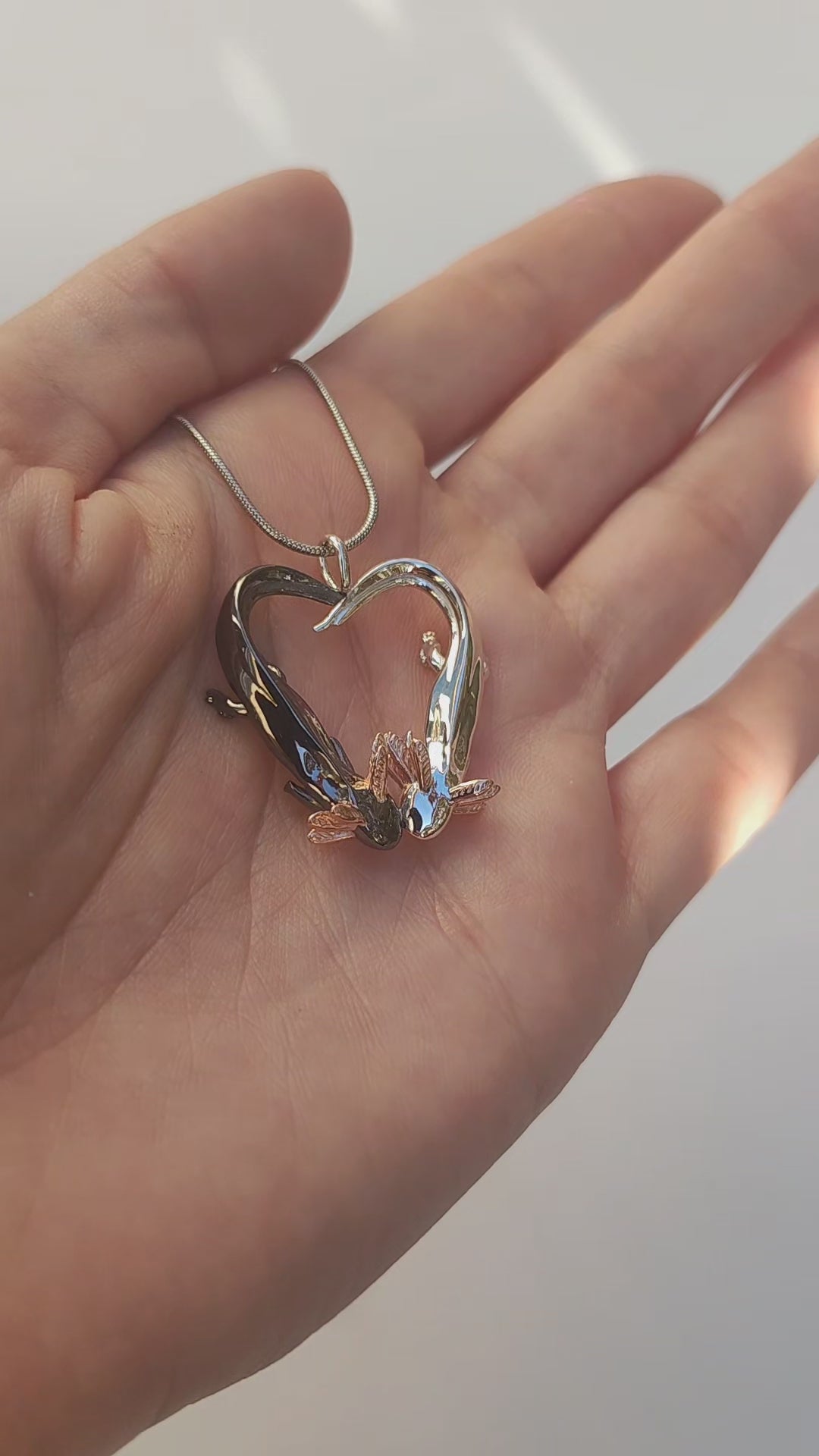 Video showing the Exolotl Love Pendant held from the front, rotating to reveal the contrast between the polished silver and black rhodium axolotls forming a heart.