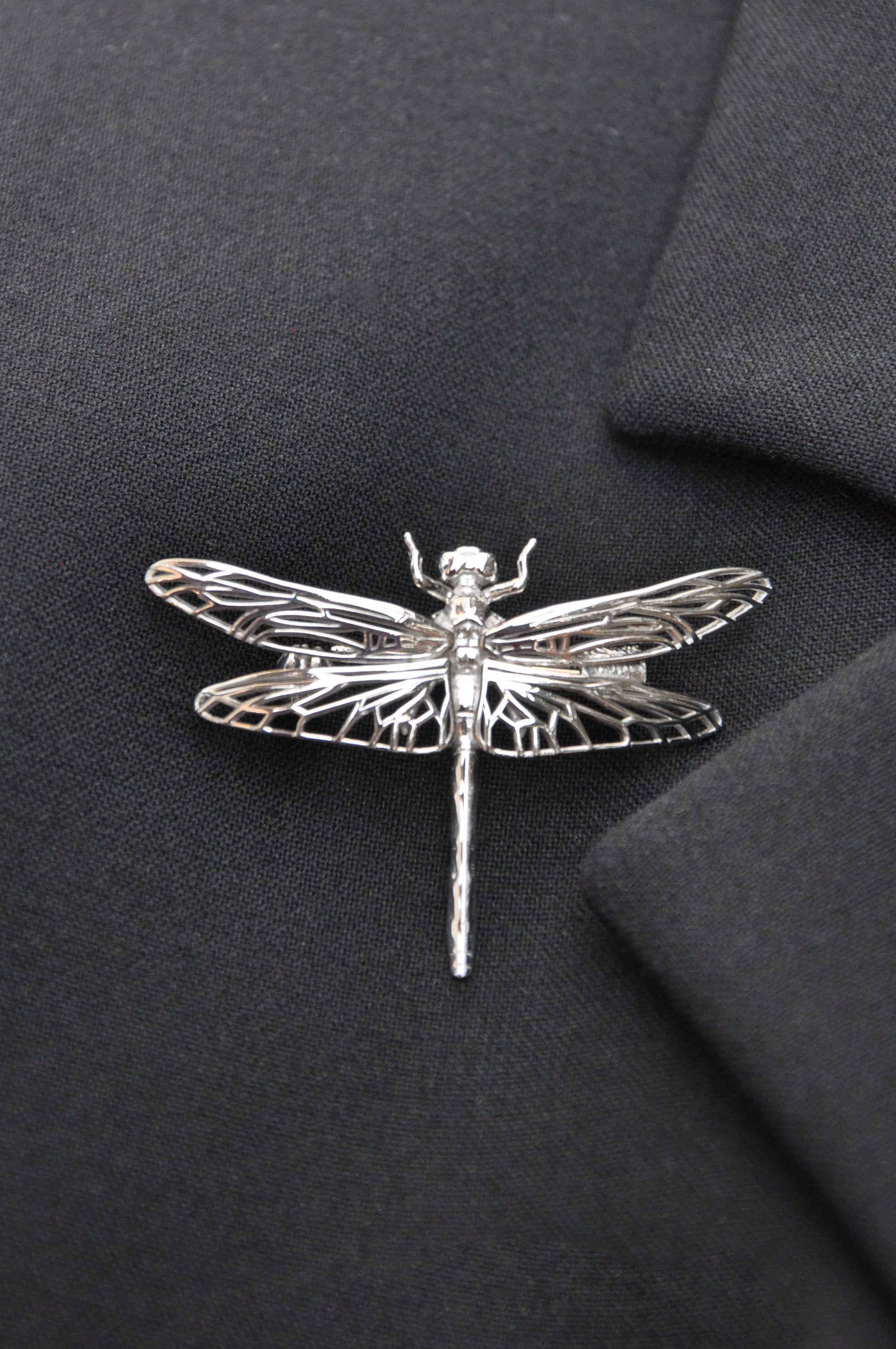 Silver dragonfly brooch pinned to black cloth, emphasizing the contrast and intricate nature-inspired design.