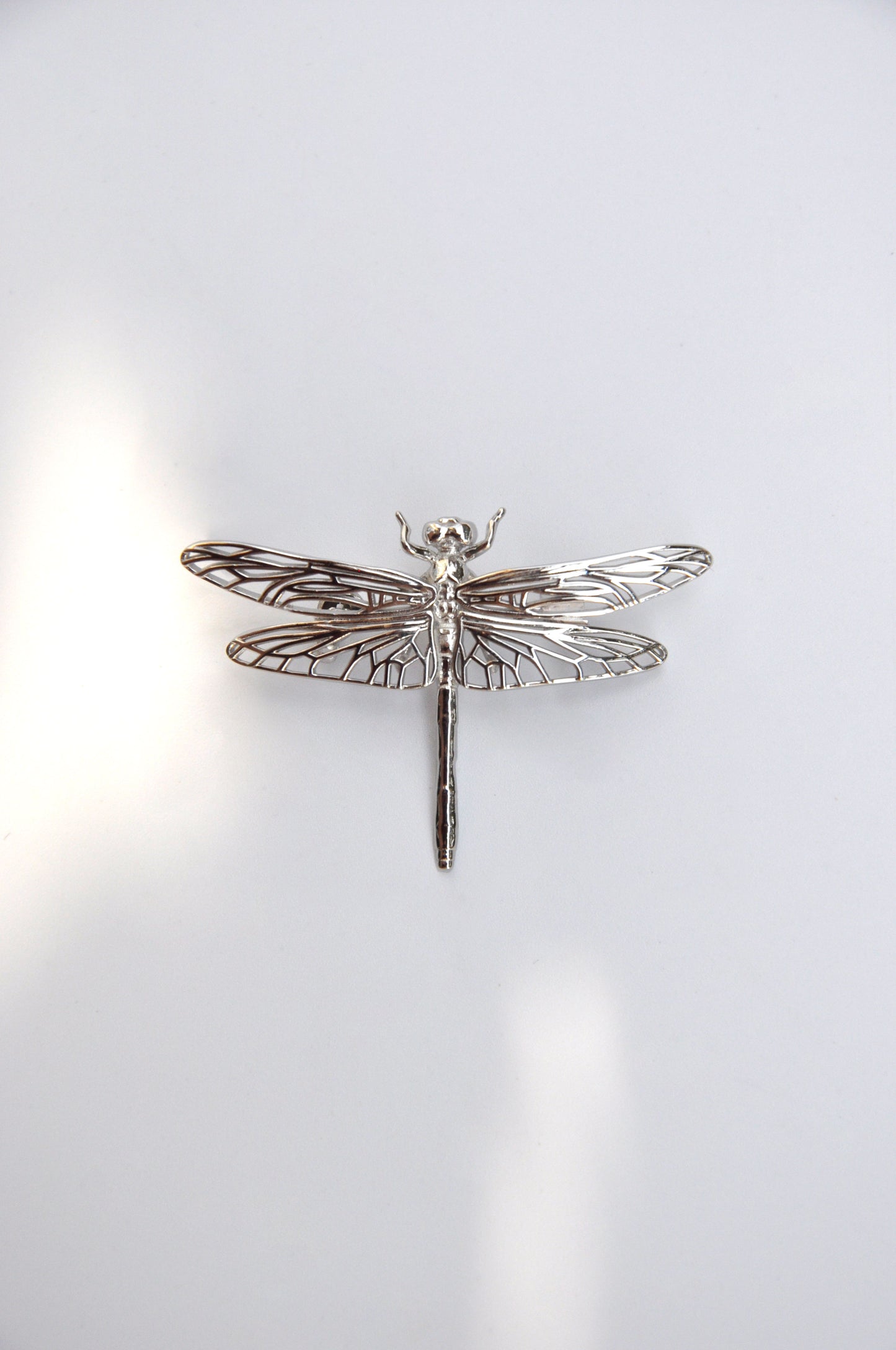 Silver dragonfly brooch on a white background, highlighting its delicate wings and handcrafted detail.
