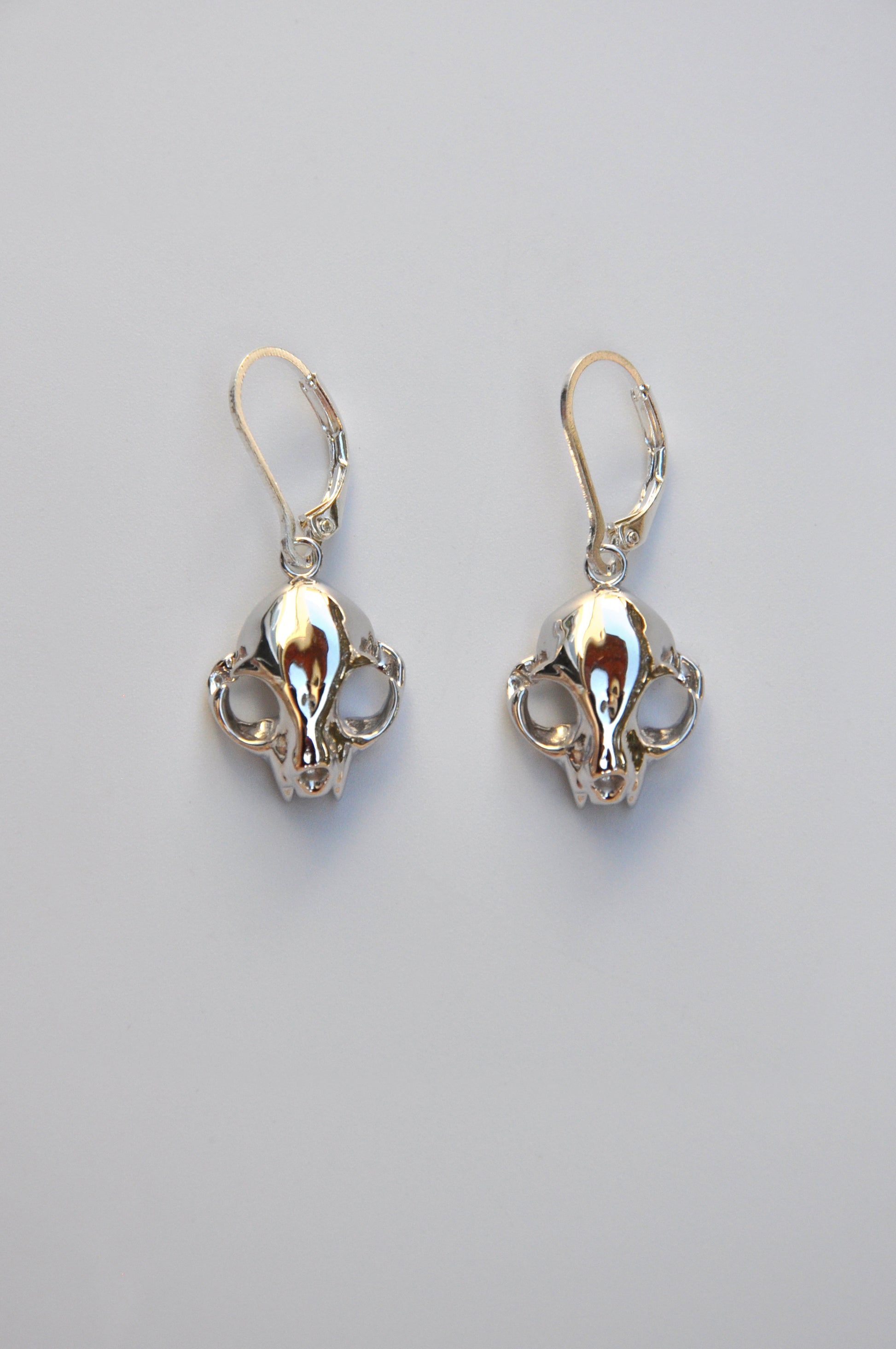 Silver feline skull dangle drop earrings displayed on a white background, showing detailed craftsmanship.