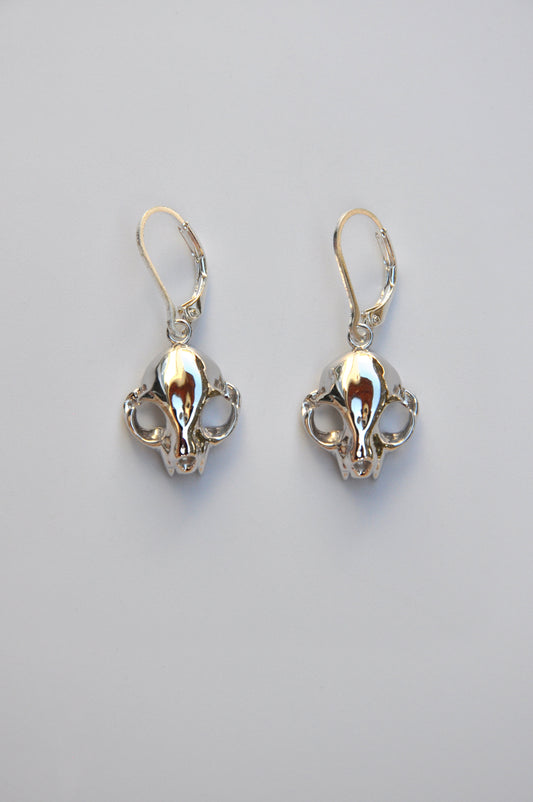 Silver feline skull dangle drop earrings displayed on a white background, showing detailed craftsmanship.