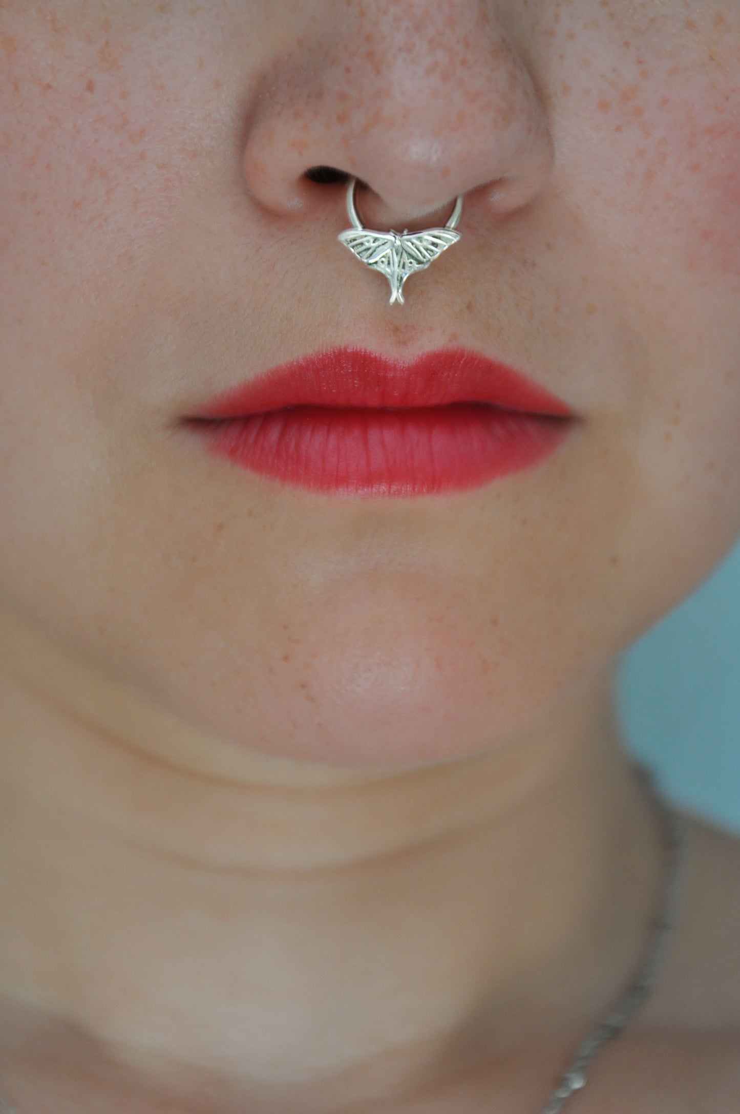 Woman wearing a handcrafted sterling silver luna moth septum ring, showcasing the delicate moth design resting on a minimalist hoop.