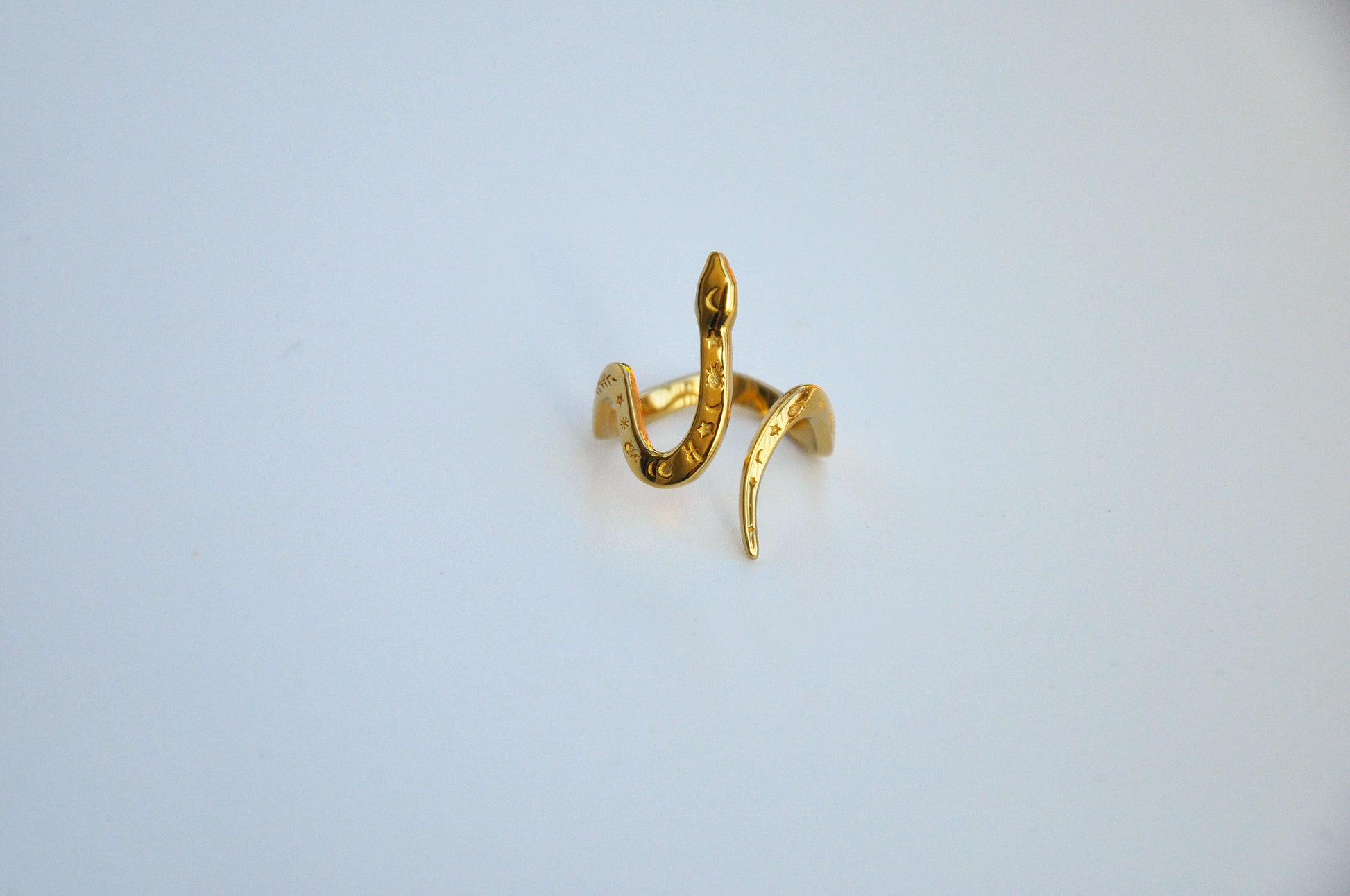 Front view of celestial snake ring in gold on white background, showing serpent head and celestial motifs.
