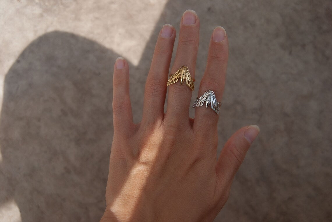 Alternate view of silver and gold sphinx moth rings stacked on hand, highlighting polished finish and wing details.