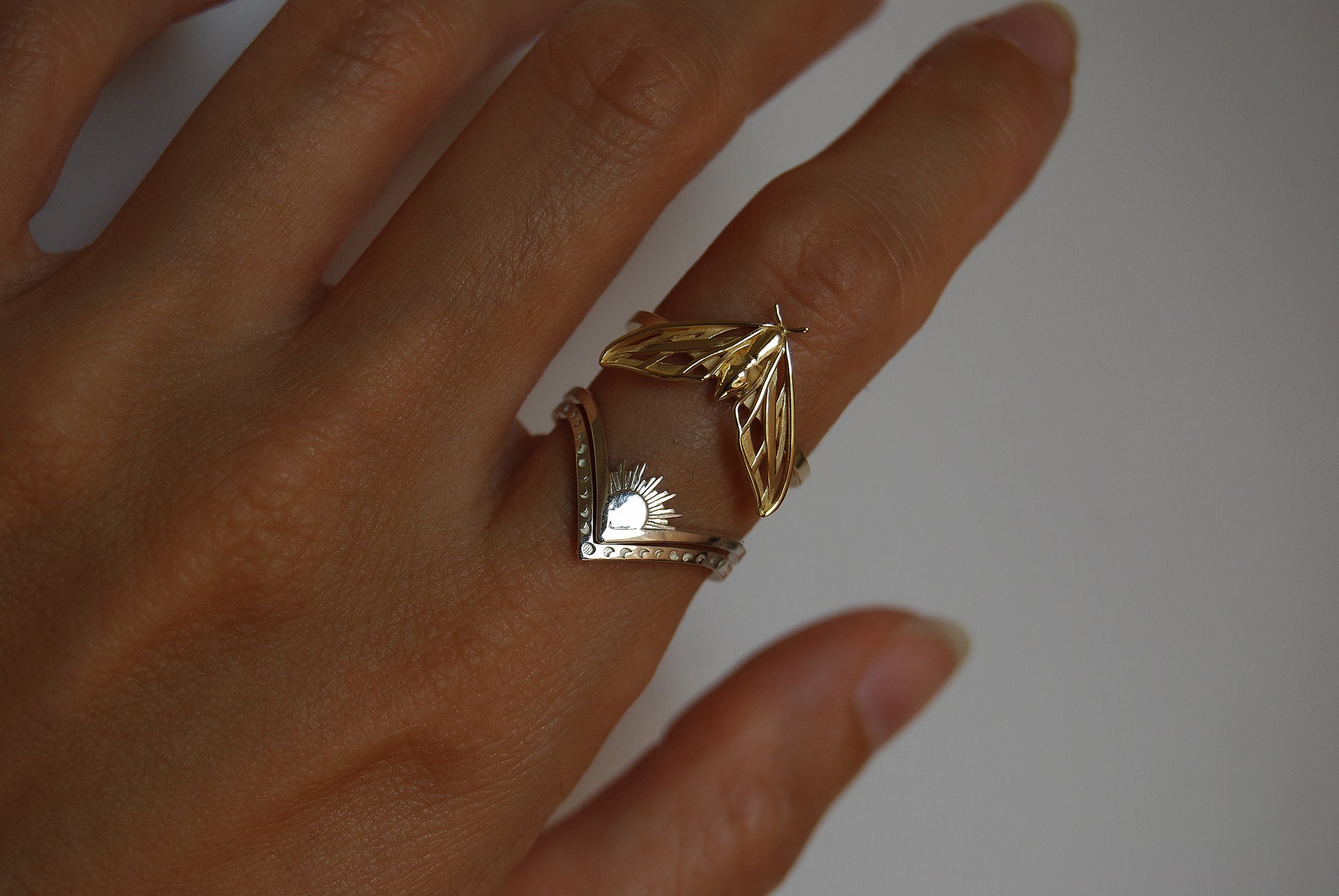 Sun and moon chevron rings stacked with moth ring, combining lunar and insect symbolism in a celestial jewelry set.