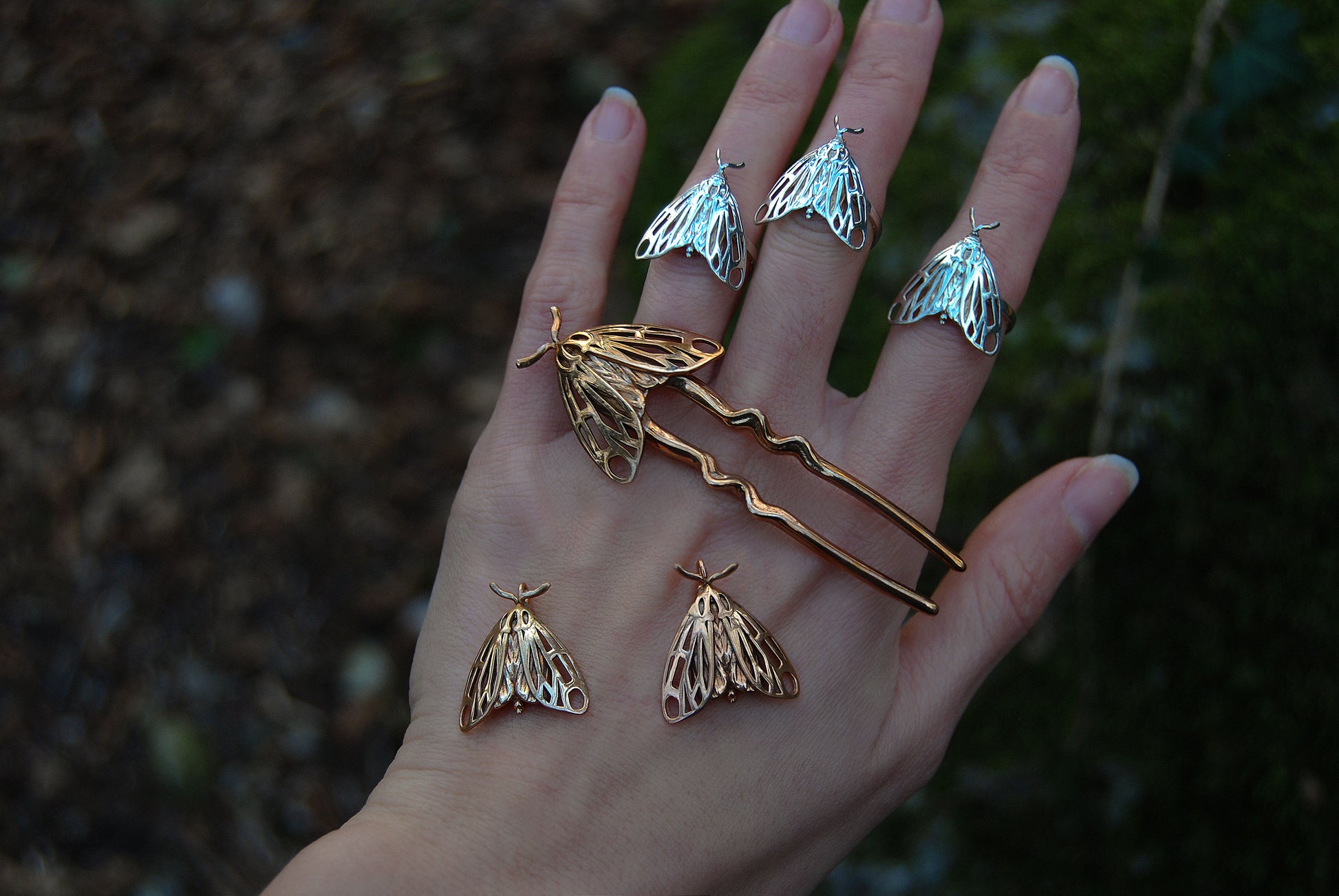 Bronze Tiger Moth hair pin displayed with silver Tiger Moth rings worn on the hand, showcasing handcrafted insect-inspired jewelry in mixed metallic finishes.