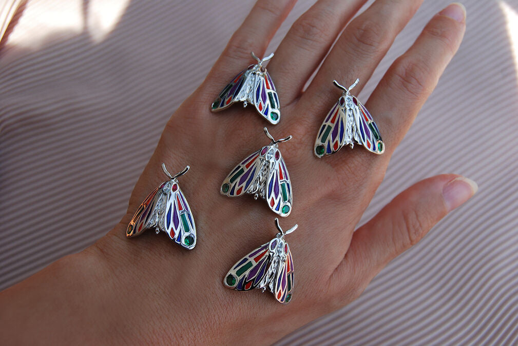 Collection of multiple jeweled Tiger Moth pendants displayed on hand