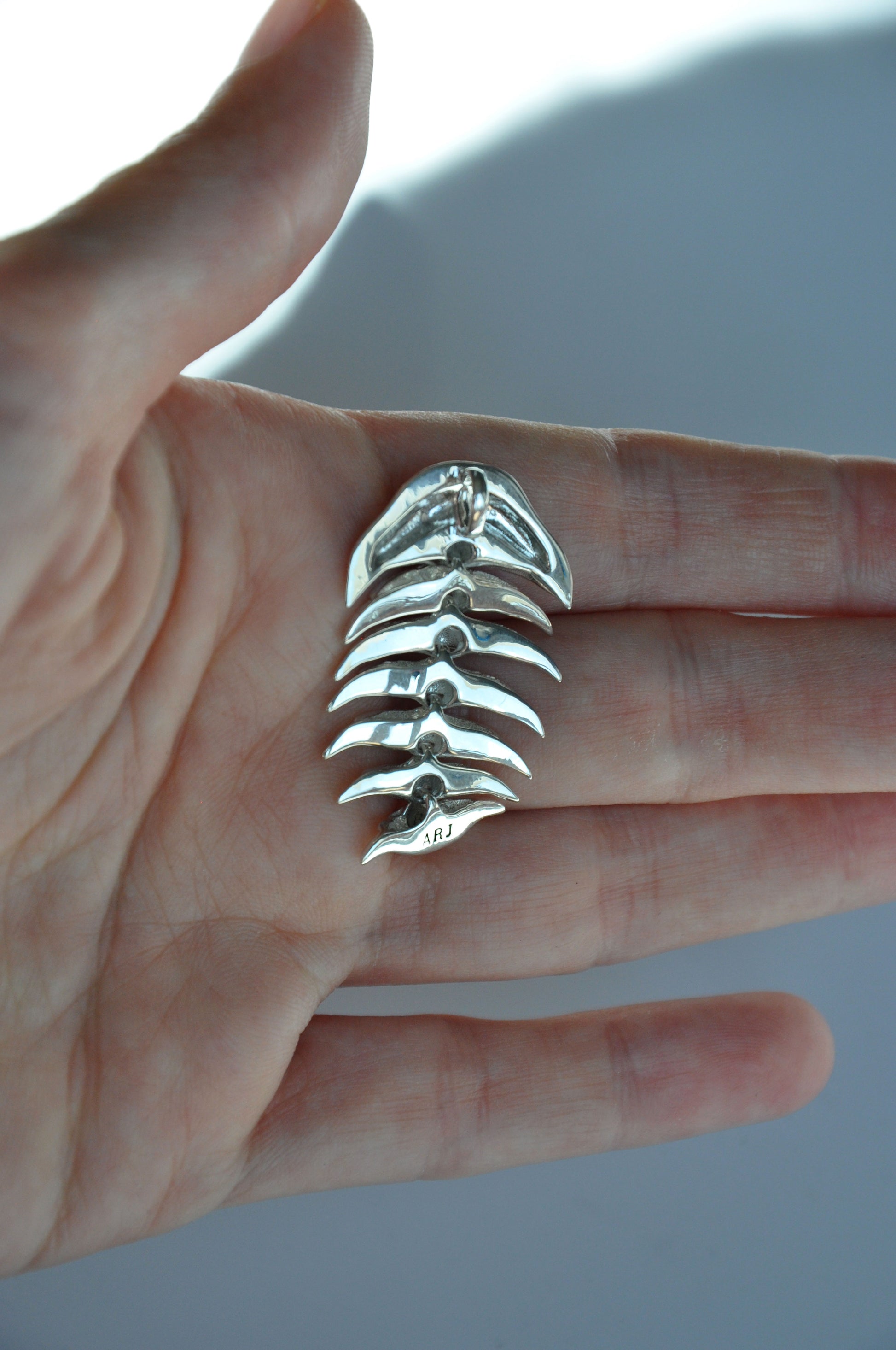 Close-up of a hand holding the back side of a sterling silver articulated trilobite pendant against a white background. The smooth, polished reverse reveals the craftsmanship behind the segmented design, emphasizing its structural detail and tactile quality.