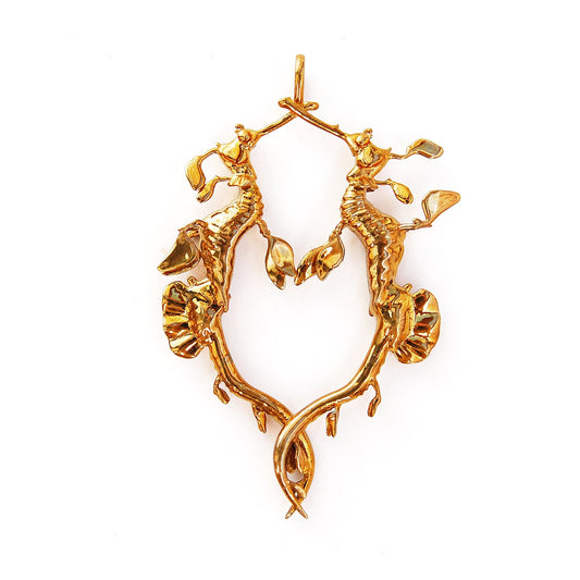 A gold-colored pendant featuring two stylized sea dragon figures in an embrace, with leaf-like appendages.