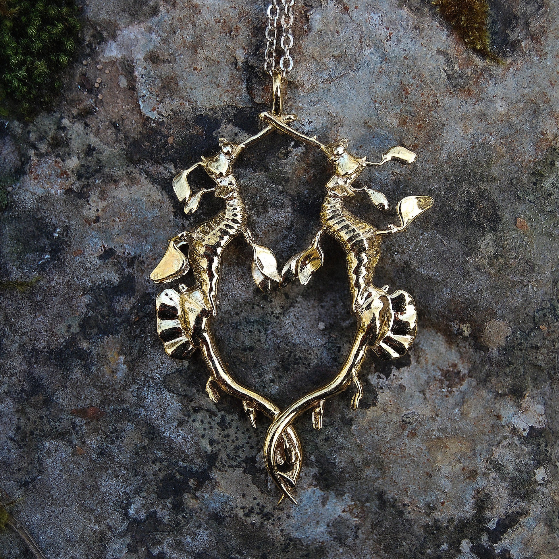 Two weedy sea dragons in a loving embrace, gold pendant symbolizing connection and marine elegance.
