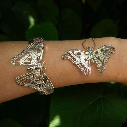 Sterling silver Atlas Moth pendant and matching bracelet worn on a hand, set against a lush nature background. The intricate moth design gleams in natural light, highlighting its delicate wing details and sculptural elegance. The organic setting enhances the jewelry’s connection to the natural world, emphasizing its inspiration from one of Earth’s largest and most beautiful moths