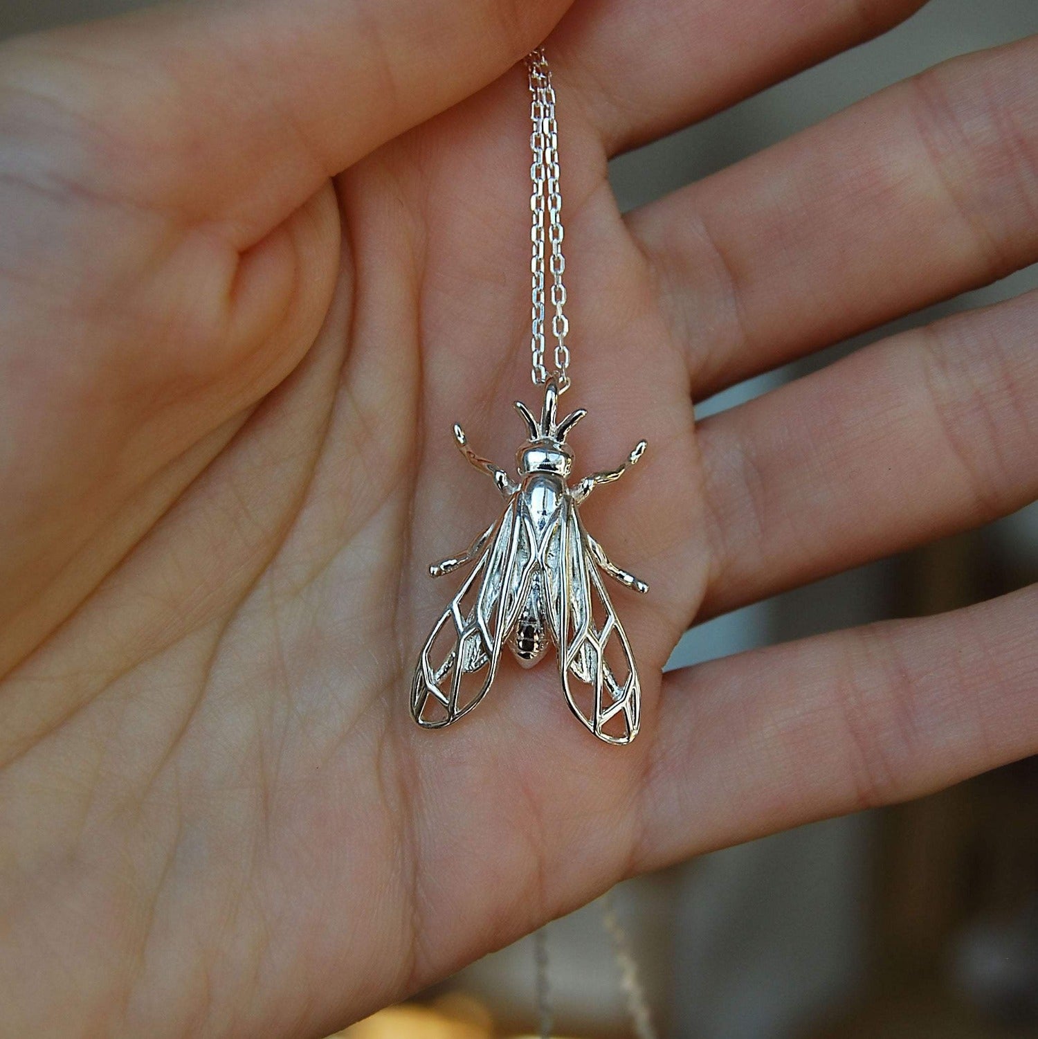 Sterling silver wasp pendant worn on hand, showcasing intricate insect details