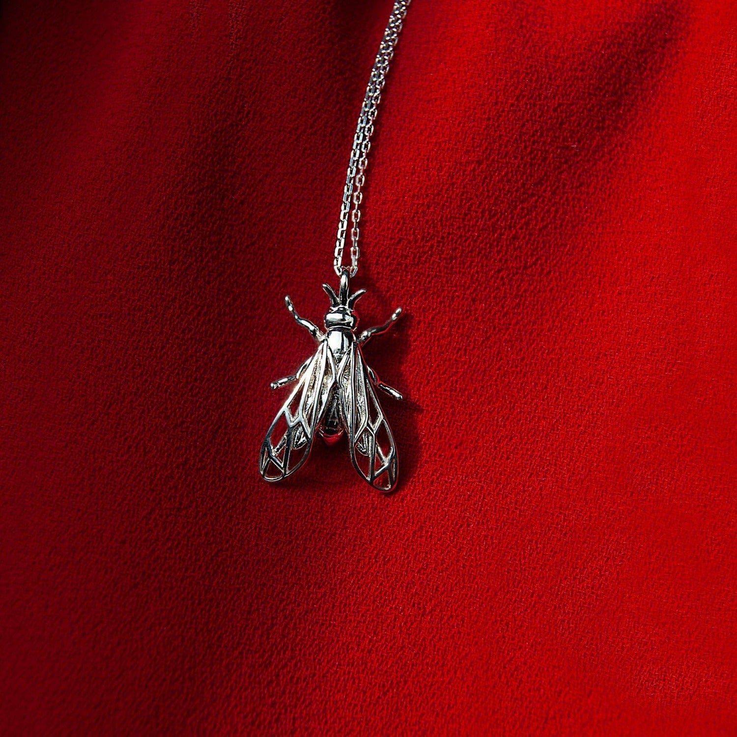 Close-up of wasp pendant on vibrant red background, insect-themed jewelry piece